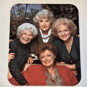 May include: A group of four women, all smiling, are pictured together. They are wearing a variety of clothing, including a green sweater, a black and white patterned shirt, a red jacket, and a blue shirt. The women are all looking at the camera.