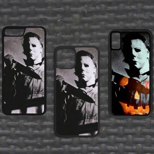 May include: Three black phone cases with different images of the horror movie character Michael Myers. The first case features a close-up of Michael Myers holding a knife. The second case features a close-up of Michael Myers holding a knife with a pumpkin in the background. The third case features a close-up of Michael Myers holding a knife with a pumpkin in the background.