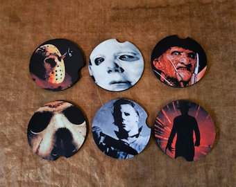 Puede incluir: Seis posavasos redondos con personajes de películas de terror. Los posavasos son negros con detalles en blanco, rojo y naranja. Los personajes incluyen a Jason Voorhees, Michael Myers, Freddy Krueger y una silueta de una figura con un cuchillo.