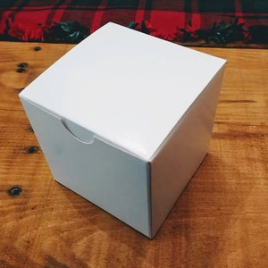 May include: A plain white square box with a smooth, matte finish and a small semi-circular cutout on the top edge of the front panel, designed for easy opening. The box is constructed from a single piece of folded cardstock material.