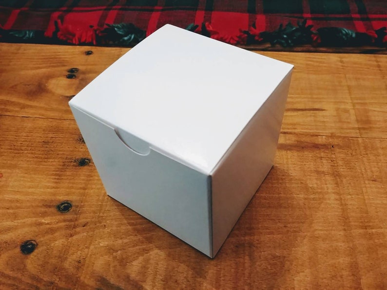 May include: A plain white square box with a smooth, matte finish and a small semi-circular cutout on the top edge of the front panel, designed for easy opening. The box is constructed from a single piece of folded cardstock material.