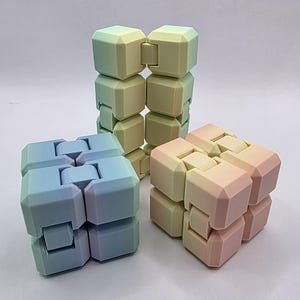 May include: Three multi-colored infinity cubes in shades of blue, yellow, and pink. The cubes are made of connected blocks that can be manipulated. The background is a plain white.