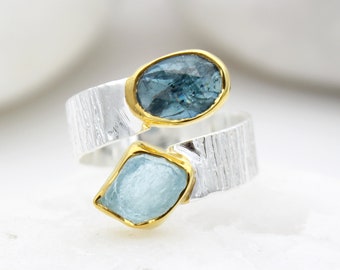 May include: A silver ring with a textured band and two blue gemstones. The ring is set with a larger oval-shaped gemstone and a smaller, diamond-shaped gemstone.