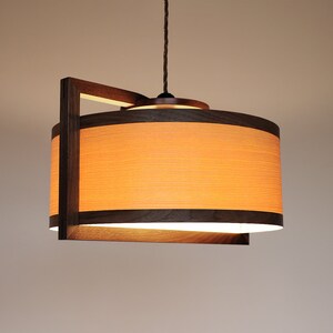 Può includere: Una lampada a sospensione in legno con un paralume curvo di colore marrone chiaro e una cornice in legno marrone scuro.