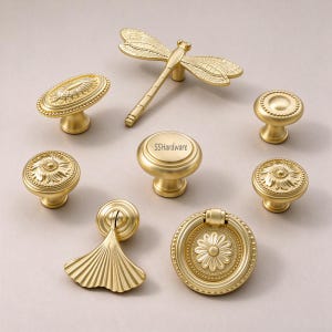 May include: A collection of eight gold-toned metal cabinet knobs and pulls in various shapes, including a dragonfly, a ginkgo leaf, and circular designs with floral patterns. One central knob features the text SSHardware printed on it.