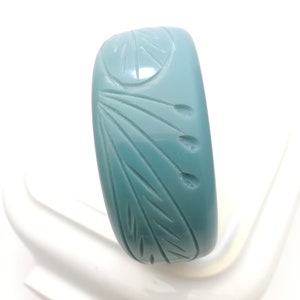 Op de afbeelding: Een turquoise brede armband met gesneden blad- en bloemmotieven. De armband heeft een gladde, glanzende afwerking en een afgeronde rechthoekige vorm. De gesneden details geven het accessoire textuur.