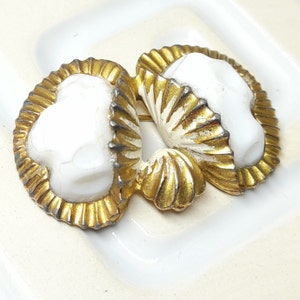 May include: A vintage brooch with a symmetrical design. It features two white, shell-like shapes with gold-coloured, textured edges. The brooch has a pin fastening. The overall aesthetic is classic and antique.