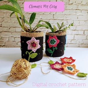 May include: Two black crochet pot cozies with gold trim and colourful flower appliqués, each holding a plant. A ball of gold yarn and a garland of crochet flowers are in the foreground. Text reads "Clematis Pot Cosy" and "Digital crochet pattern."