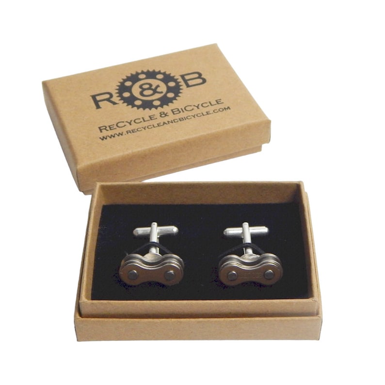 May include: A pair of silver cufflinks in a brown box. The cufflinks are shaped like a bicycle chain and have a black rubber band. The box is labeled "R&B Recycle & Bicycle www.recycleandbicycle.com"