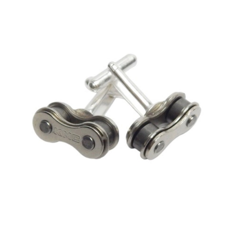 May include: A pair of silver cufflinks with a black bike chain design. The chain links are connected to the cufflink backs.