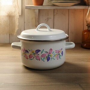 May include: White enamel pot with lid, featuring a floral design in pink, purple, and yellow. The pot has two side handles and a loop handle on the lid. The kitchenware is set against a rustic wooden backdrop.