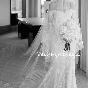 May include: A bride wearing a white lace wedding dress with a long veil and holding a bouquet of white flowers. The text "Veils by Rebecca" is visible in the image.