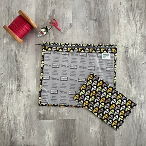 Pode incluir: Uma bolsa transparente com fecho de correr de pl&aacute;stico com um forro de tecido preto e amarelo com um padr&atilde;o repetido dos personagens do programa de televis&atilde;o "The Office". A bolsa est&aacute; aberta e uma bolsa de tecido mais pequena de cor preta e amarela com o mesmo padr&atilde;o est&aacute; dentro.