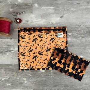 Pode incluir: Duas bolsas de z&iacute;per de tecido com temas de Halloween. Uma bolsa apresenta um padr&atilde;o preto e laranja de morcegos sobre um fundo bege. A outra bolsa apresenta um padr&atilde;o preto e laranja de l&aacute;pides e cruzes sobre um fundo bege.