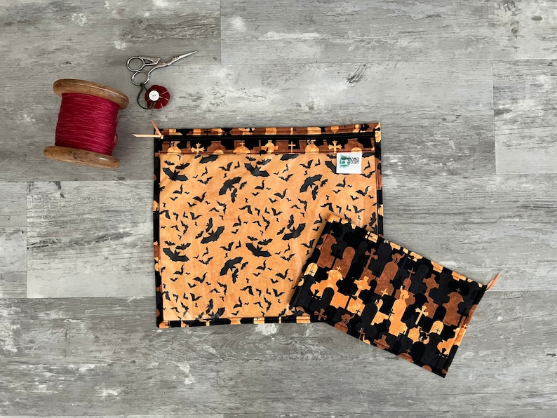 Pode incluir: Duas bolsas de z&iacute;per de tecido com temas de Halloween. Uma bolsa apresenta um padr&atilde;o preto e laranja de morcegos sobre um fundo bege. A outra bolsa apresenta um padr&atilde;o preto e laranja de l&aacute;pides e cruzes sobre um fundo bege.