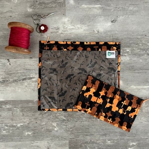 Pode incluir: Duas bolsas com fecho de correr em tecido com tema de Halloween. Uma bolsa &eacute; preta com silhuetas laranja e castanhas de l&aacute;pides e cruzes. A outra bolsa &eacute; preta com silhuetas cinzentas de morcegos. Ambas as bolsas t&ecirc;m janelas de pl&aacute;stico transparente.