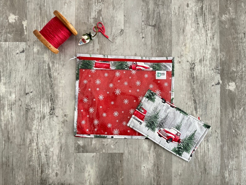 Pode incluir: Duas bolsas transparentes com z&iacute;per com padr&otilde;es de flocos de neve vermelhos e brancos e uma cena de inverno com um caminh&atilde;o vermelho e pinheiros. A bolsa maior tem uma etiqueta verde com o texto "Sewing Shop".