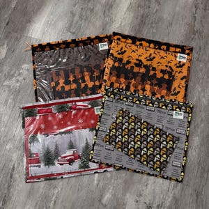 Pode incluir: Quatro bolsas com z&iacute;per diferentes com v&aacute;rios designs. As bolsas s&atilde;o feitas de tecido e t&ecirc;m uma janela de pl&aacute;stico transparente. Os designs incluem uma &aacute;rvore de Natal e um caminh&atilde;o, um cemit&eacute;rio com morcegos, um padr&atilde;o de trabalhadores de escrit&oacute;rio e um padr&atilde;o de trabalhadores de escrit&oacute;rio com o texto "Dunder Mifflin" repetido.