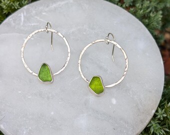 May include: A pair of silver hoop earrings with hammered texture, each featuring a green sea glass piece.