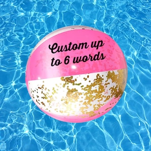 May include: Pink and white beach ball with gold glitter. The ball has the text "Custom up to 6 words" printed on it.