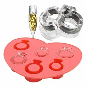 May include: Pink silicone mold with six ring-shaped cavities. The mold is shaped like a heart.  The rings have a diamond-shaped design in the center.  There are two clear plastic rings with a diamond-shaped design in the center.