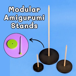 May include: Three black circular stands with vertical wooden dowels of varying heights. A circular inset shows a green disc with a center hole and a separate wooden dowel. The text Modular Amigurumi Stands is displayed in white.