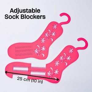 May include: Two bright pink adjustable sock blockers with a floral cutout pattern and a hanging hook. The text Adjustable Sock Blockers is visible. A black arrow indicates a length of 25 cm for the foot section of the sock blocker.