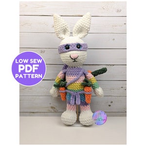 May include: Crochet pattern for a white bunny wearing a purple and rainbow ninja costume holding carrots. The pattern is called "Low Sew PDF Pattern".