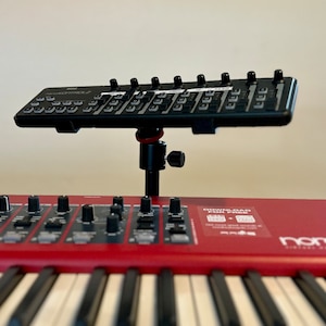 May include: A black Korg nanoKONTROL2 MIDI controller mounted above a red Nord keyboard. The keyboard has white keys and black controls. The image is a close-up of the musical instruments.