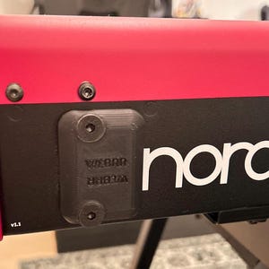 May include: Close-up of a black keyboard with a red top. The keyboard has a white "Nord" logo and a black plastic cover with the word "WEBER" printed on it.