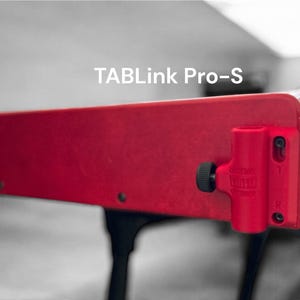 May include: A close-up of a red rectangular object with the text "TABLink Pro-S" in white. The object has a black knob and a red cylindrical component attached to it. The background is blurred.
