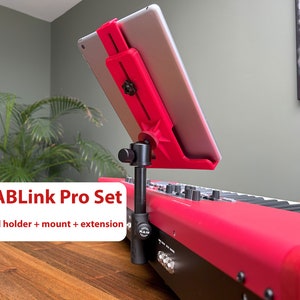 Op de afbeelding: Een rode iPad-houder met een zwarte houder en een verlengarm bevestigd aan een rood toetsenbord. De tekst "TABLink Pro Set" en "iPad holder + mount + extension" is zichtbaar op het toetsenbord.