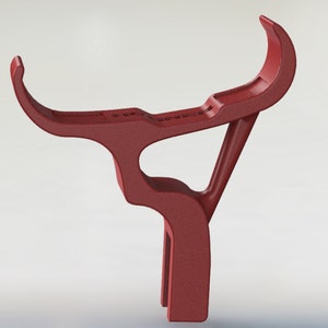 Puede incluir: Un soporte de tel&eacute;fono de pl&aacute;stico rojo con un dise&ntilde;o curvo. El soporte est&aacute; dise&ntilde;ado para sostener un tel&eacute;fono en posici&oacute;n vertical.