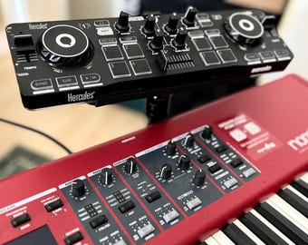 Puede incluir: Un controlador DJ Hercules negro con una rueda de jog y botones está montado en la parte superior de un teclado Nord Stage 3 rojo.