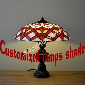 May include: A red and white stained glass table lamp with a geometric pattern. The lamp has a bronze base and a white shade.