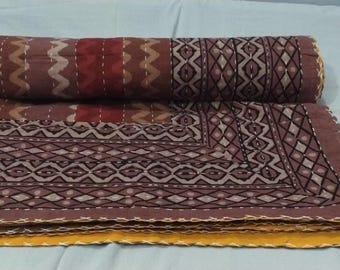 Puede incluir: Una colcha kantha marrón y beige con un patrón geométrico. La colcha está doblada por la mitad y tiene un borde amarillo.