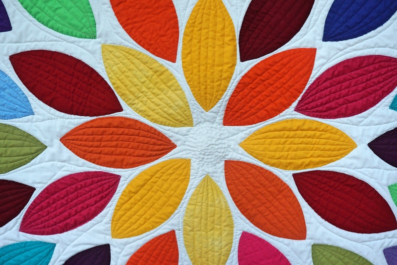 Pu&ograve; includere: Un quilt colorato con un design circolare di forme di foglie sovrapposte in tonalit&agrave; di rosso, arancione, giallo, verde, blu e viola.