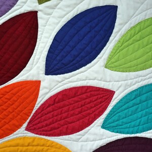 Pu&ograve; includere: Un quilt colorato con un motivo di foglie sovrapposte in tonalit&agrave; di rosso, arancione, giallo, verde, blu e viola. Le foglie sono trapuntate con un punto decorativo.