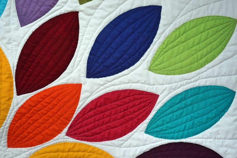 Pu&ograve; includere: Un quilt colorato con un motivo di foglie sovrapposte in tonalit&agrave; di rosso, arancione, giallo, verde, blu e viola. Le foglie sono trapuntate con un punto decorativo.