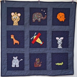 May include: A blue and white quilted baby blanket with various animal and airplane appliques. The animals include a giraffe, zebra, elephant, lion, and hippopotamus. The airplane is yellow with red wings and the text "Flying" on the side.