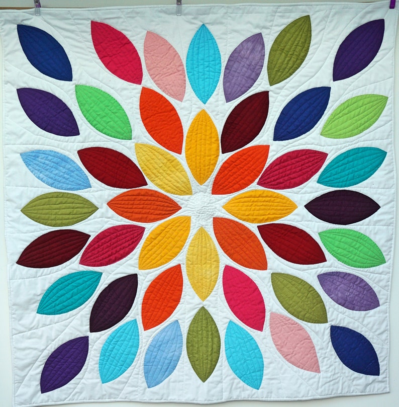 Pu&ograve; includere: Un quilt colorato con un design circolare di forme di foglie sovrapposte in tonalit&agrave; di rosso, arancione, giallo, verde, blu, viola e rosa.