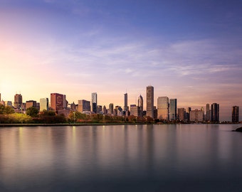 May include: A panoramic view of the Chicago skyline at sunset, with the city's skyscrapers reflected in the calm waters of Lake Michigan.