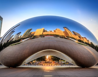 May include: A large, shiny, silver sculpture in the shape of a bean reflects the city skyline in Chicago, Illinois. The sculpture is in a public park with a paved area in front of it.