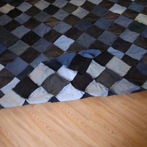 May include: A handmade quilt featuring a patchwork design of diamond-shaped denim squares in shades of blue and black. The quilt is displayed on a wooden floor, showcasing its texture and color variations.