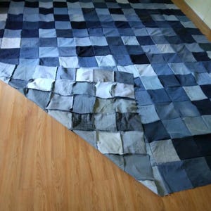 May include: A large, handmade denim quilt composed of numerous square patches in varying shades of blue. The quilt is laid out on a wooden floor, showcasing its patchwork design and texture. The quilt's dimensions are approximately 72 x 84 inches.