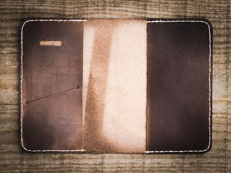 May include: A brown leather wallet with a white stitch detail and a light brown leather flap. The wallet has a pocket on the left side and a flap on the right side.