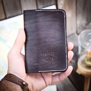 May include: A brown leather wallet with white stitching and the text "TEDPERE" and a logo of an anchor with a circle around it.