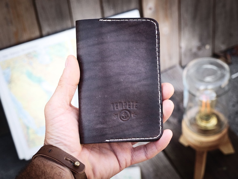 May include: A brown leather wallet with white stitching and the text "TEDPERE" and a logo of an anchor with a circle around it.