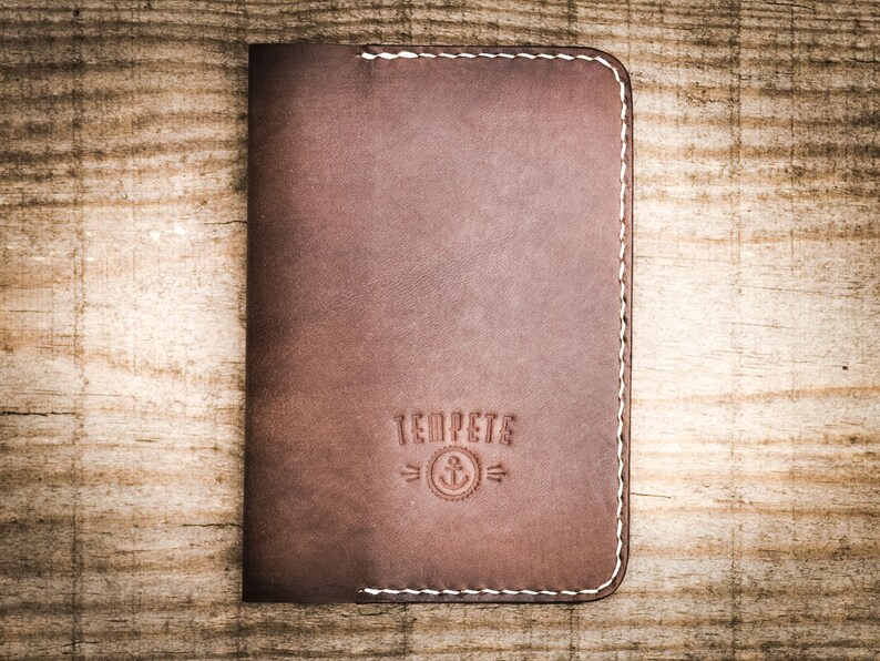 May include: A brown leather wallet with white stitching and the text "Temp&ecirc;te" with an anchor symbol.