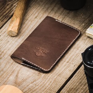 May include: A brown leather passport holder with white stitching and the word "Voyage" embossed on the front.
